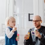 A joyful moment between a father and daughter blowing bubbles indoors, highlighting family fun.