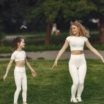 Mother and daughter bonding through outdoor exercise in activewear, featuring a joyful moment in a green park.